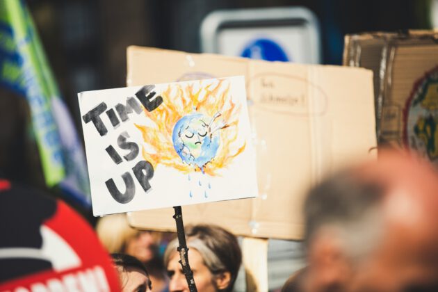 Auf einem Plakat ist der brennende Planet Erde zu sehen. Das Plakat ist beschriftet mit "Time is up".